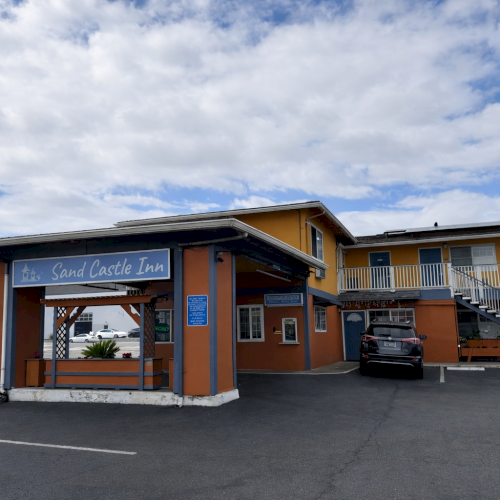 A modern, single-story house with a stone-and-wood fa&ccedil;ade, open front porch, clear blue sky, and manicured front yard.