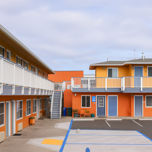 A bright orange and white building with a courtyard, walkway, and clear sky, looking like a school or campus.