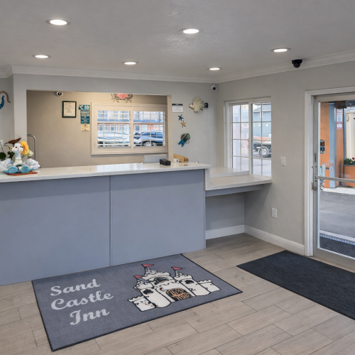 A bright, modern kitchen and living space with light wood cabinets, a central island, gray walls, and a stylish entry rug.