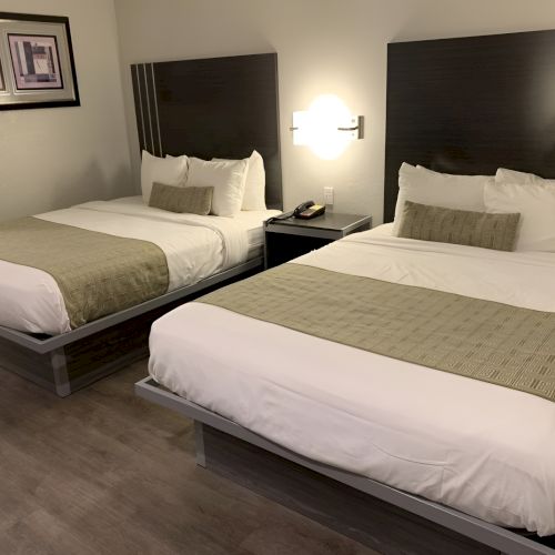 Two neatly made hotel beds with white linens and beige runners, dark headboards, and bedside lamps in a cozy, modern room.
