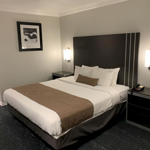 A hotel room with two twin beds pushed together, a dark headboard, nightstands, a framed wall art, and minimalist decor, ending with a word.