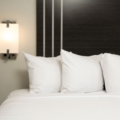 A neatly made bed with white pillows, a dark headboard, and a modern wall-mounted lamp beside it.