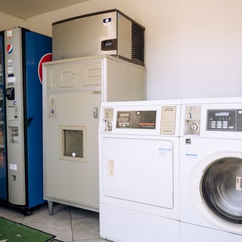 A small laundry room with a vending fridge, a beer machine, and white washing machines.