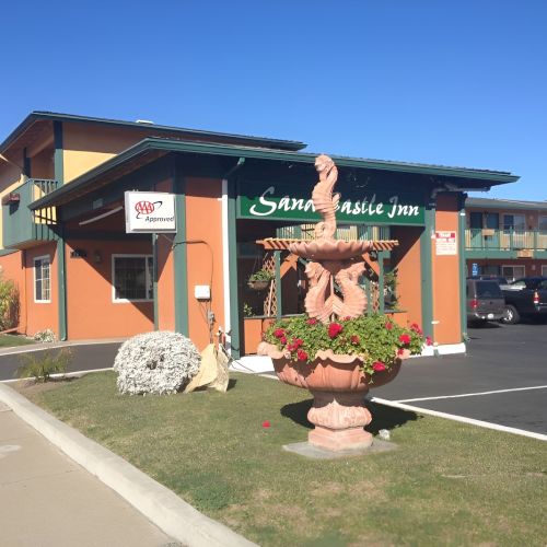 A colorful storefront with a curved awning, floral planters, and a bright mural-style sign on a sunny day.