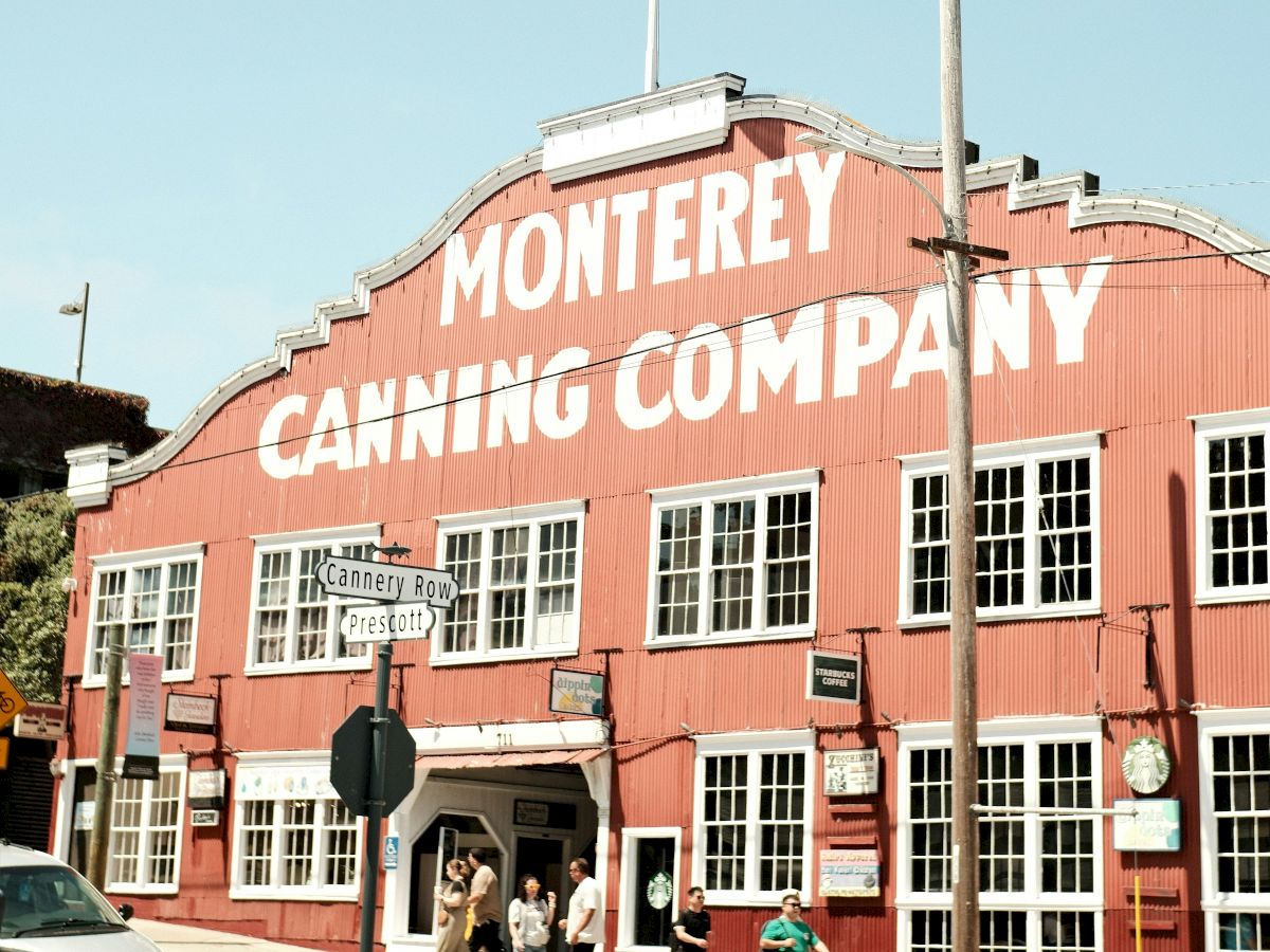 A red brick building with white-framed windows labeled &ldquo;MONTEREY CANNING COMPANY&rdquo; under a clear blue sky, people entering the entrance.