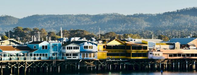 A seaside town with colorful houses along the waterfront, calm water, and hills in the background, bright and sunny day.