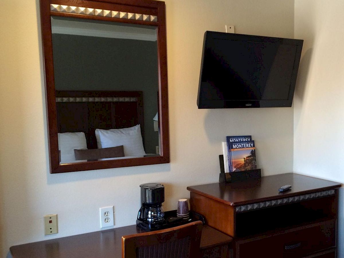 A hotel-style hotel room desk area with a mirror, coffee/tea setup, a wall-mounted TV, dresser, and a door leading to a bathroom.